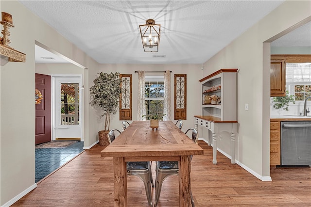 dining room featuring an inviting chandelier, a textured ceiling, sink, and light wood-type flooring