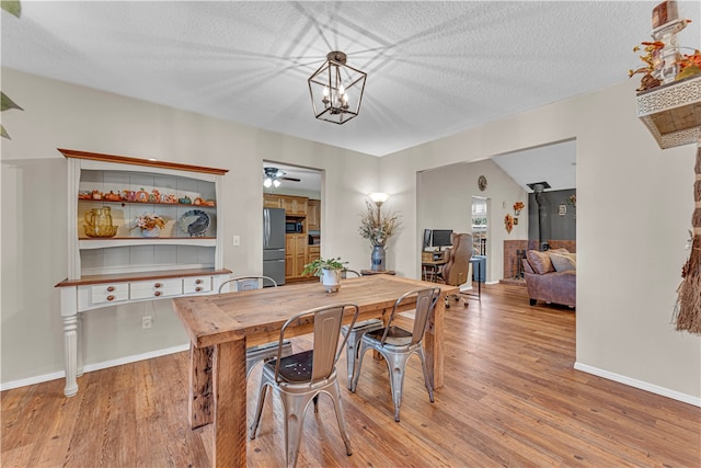 dining space with light hardwood / wood-style floors, ceiling fan with notable chandelier, a textured ceiling, and vaulted ceiling