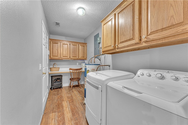 clothes washing area with a textured ceiling, light hardwood / wood-style floors, cabinets, and washer and dryer