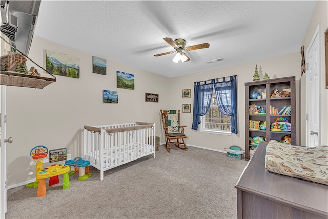 carpeted bedroom featuring ceiling fan, a textured ceiling, and a nursery area