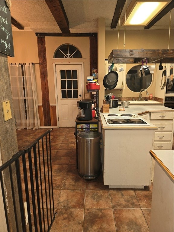 kitchen featuring beam ceiling, sink, white cabinets, and white cooktop