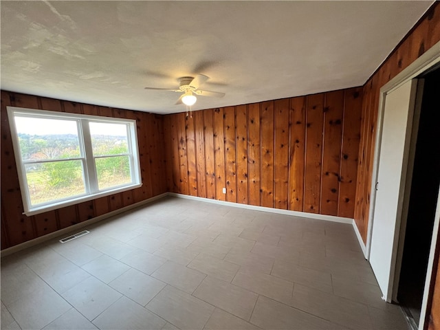 spare room featuring ceiling fan and wooden walls