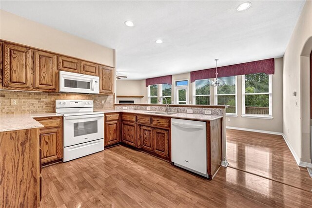 kitchen featuring white appliances, hanging light fixtures, kitchen peninsula, decorative backsplash, and sink