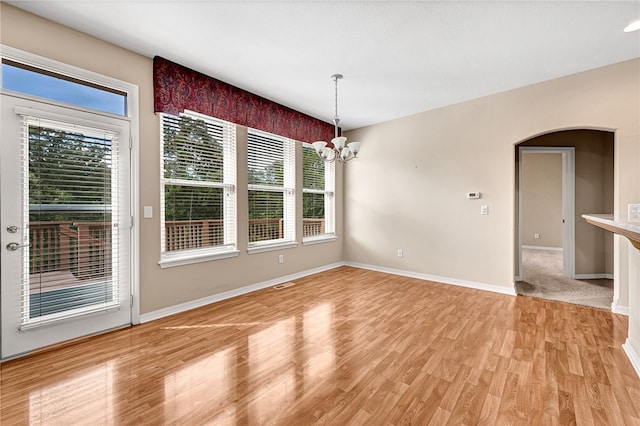 unfurnished dining area with arched walkways, a chandelier, visible vents, baseboards, and light wood-style floors