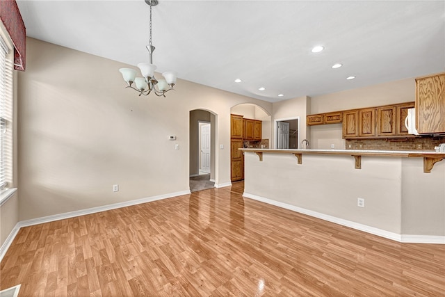 unfurnished living room with baseboards, arched walkways, an inviting chandelier, light wood-type flooring, and recessed lighting