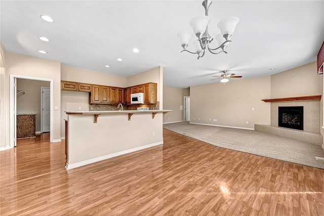 kitchen with brown cabinets, white microwave, a kitchen breakfast bar, and light wood finished floors