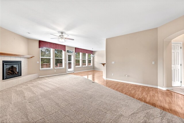 unfurnished living room with a fireplace, baseboards, arched walkways, and a ceiling fan