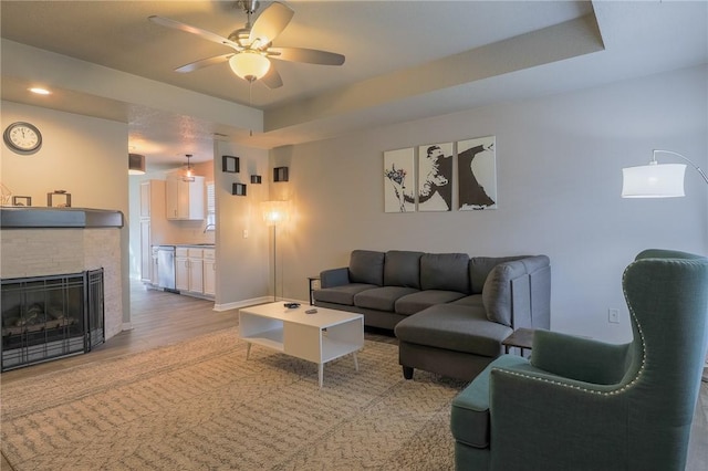 living room featuring ceiling fan, light wood-type flooring, and a raised ceiling