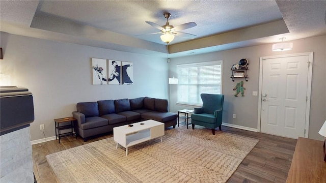 living room with a raised ceiling, ceiling fan, a textured ceiling, and hardwood / wood-style floors