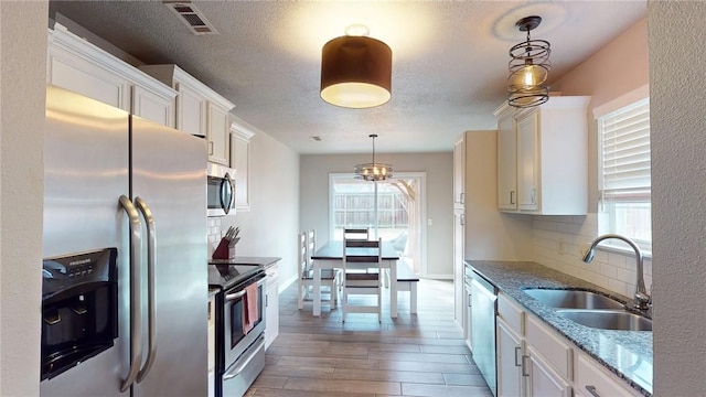 kitchen featuring light stone countertops, pendant lighting, white cabinetry, stainless steel appliances, and sink