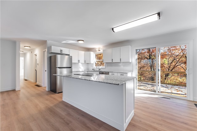 kitchen featuring stainless steel appliances, a kitchen island, light stone countertops, white cabinetry, and light hardwood / wood-style flooring