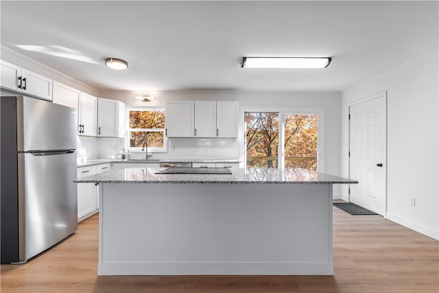 kitchen with stainless steel fridge, white cabinetry, light stone counters, and a center island