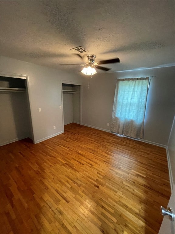 unfurnished bedroom with light wood-type flooring, a textured ceiling, two closets, and ceiling fan