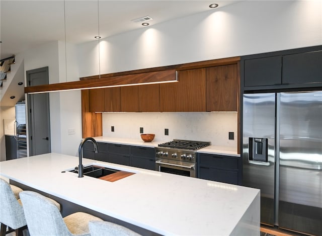 kitchen with a center island with sink, sink, a breakfast bar, appliances with stainless steel finishes, and pendant lighting