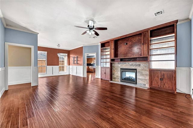 unfurnished living room featuring dark wood-type flooring, ceiling fan, ornamental molding, and a stone fireplace