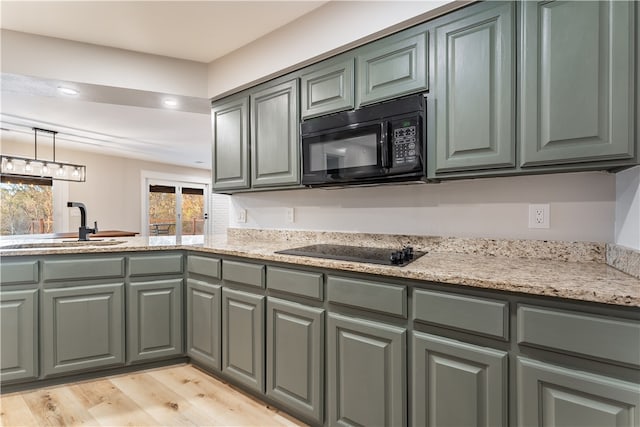 kitchen featuring light hardwood / wood-style floors, hanging light fixtures, black appliances, sink, and light stone countertops