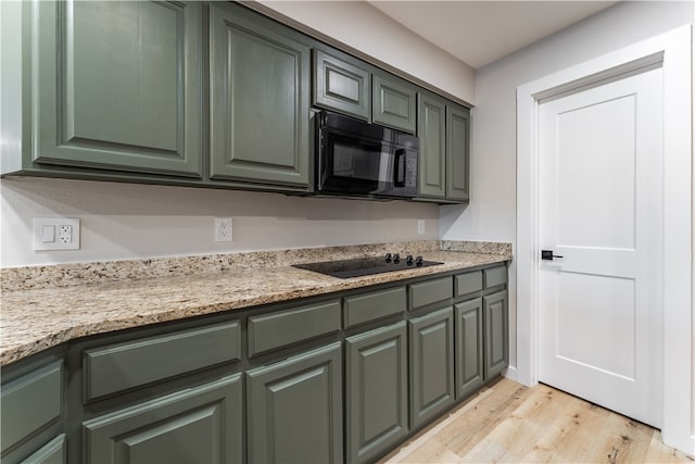 kitchen with light wood-type flooring, light stone counters, black appliances, and green cabinetry