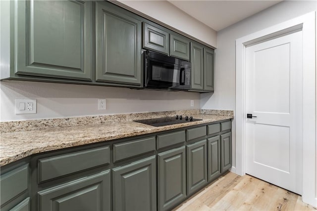 kitchen featuring gray cabinetry, black appliances, light wood-style floors, and light stone counters
