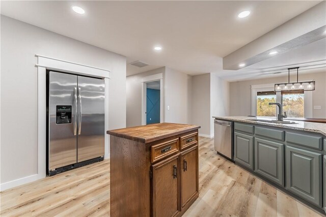 kitchen with stainless steel appliances, light hardwood / wood-style floors, a center island with sink, sink, and light stone counters