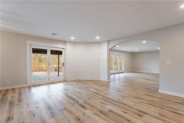 empty room with light wood-style flooring, visible vents, arched walkways, and brick wall