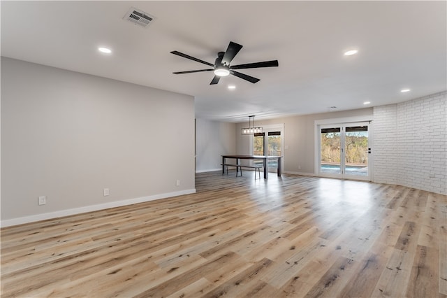 interior space featuring ceiling fan with notable chandelier, light hardwood / wood-style floors, and brick wall