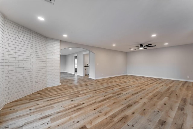 empty room featuring a ceiling fan, arched walkways, brick wall, and wood finished floors