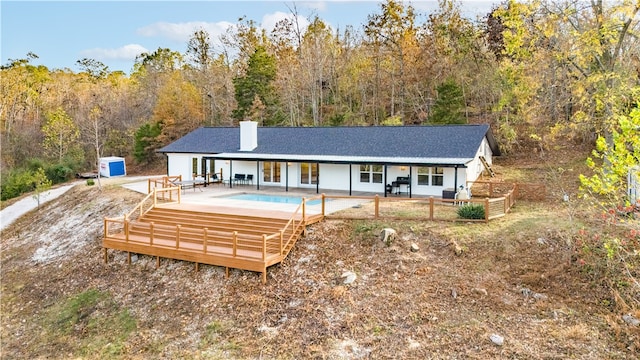 back of property featuring an outdoor pool, a chimney, roof with shingles, a forest view, and a patio area