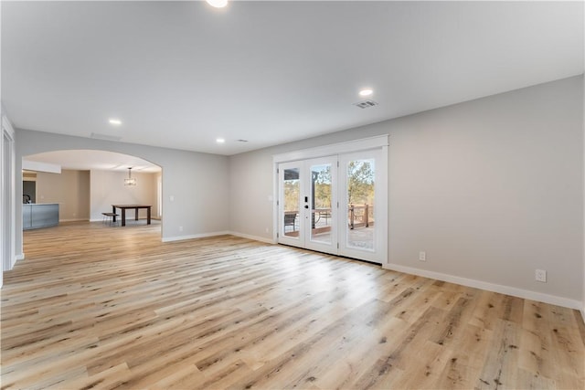 unfurnished room featuring baseboards, visible vents, arched walkways, and light wood-style floors