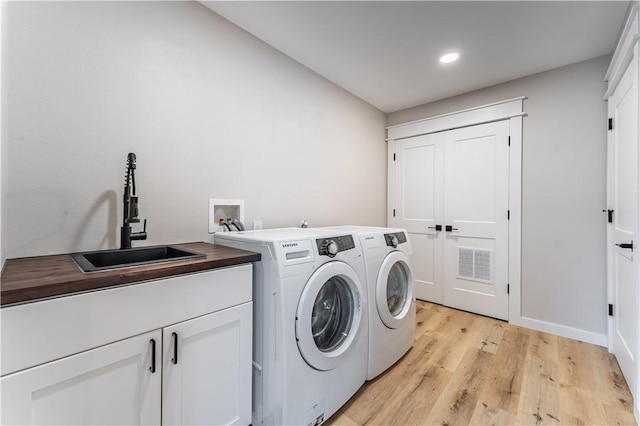 washroom with a sink, washing machine and clothes dryer, light wood-type flooring, visible vents, and cabinet space