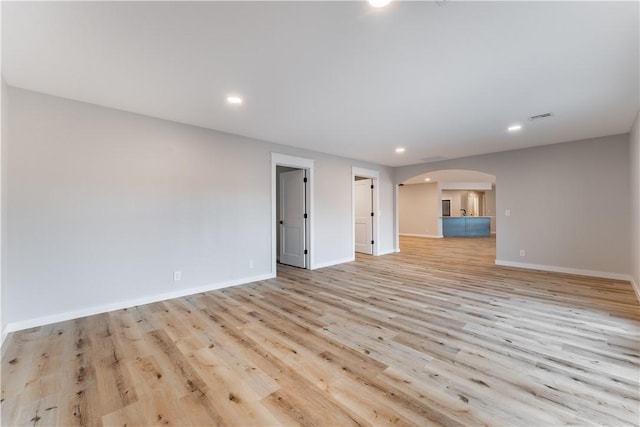 unfurnished living room featuring recessed lighting, arched walkways, baseboards, and light wood-type flooring