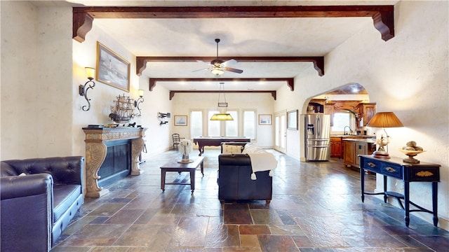 living room featuring beamed ceiling, sink, ceiling fan, a fireplace, and billiards