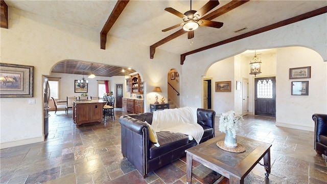 living room featuring a wealth of natural light, ceiling fan with notable chandelier, and beam ceiling