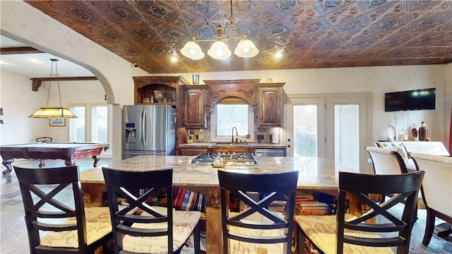 kitchen with sink, appliances with stainless steel finishes, light stone countertops, hanging light fixtures, and a kitchen island