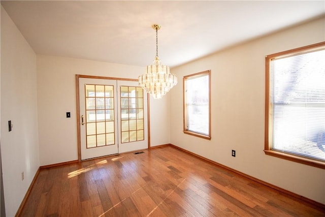 unfurnished dining area with wood-type flooring and a notable chandelier