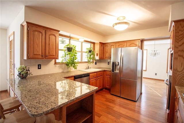 kitchen featuring kitchen peninsula, light wood-type flooring, light stone countertops, a breakfast bar, and stainless steel appliances