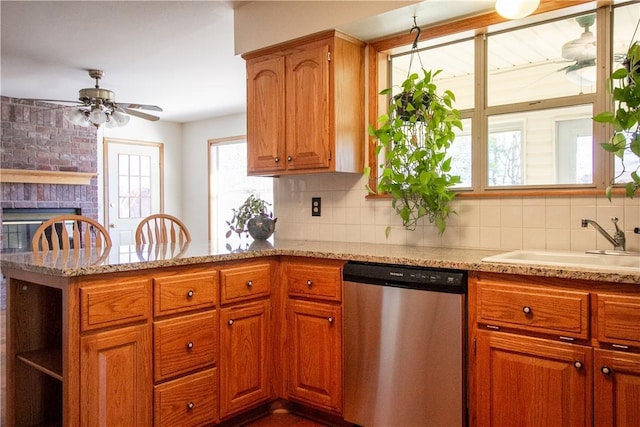 kitchen featuring a brick fireplace, stainless steel dishwasher, sink, kitchen peninsula, and backsplash