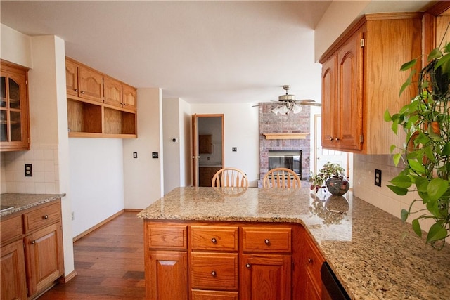 kitchen featuring tasteful backsplash, a brick fireplace, dark wood-type flooring, ceiling fan, and light stone counters