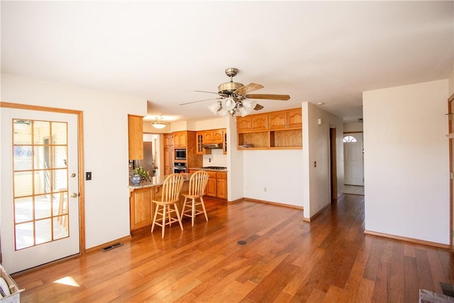 kitchen with ceiling fan, stainless steel microwave, light wood-type flooring, kitchen peninsula, and backsplash