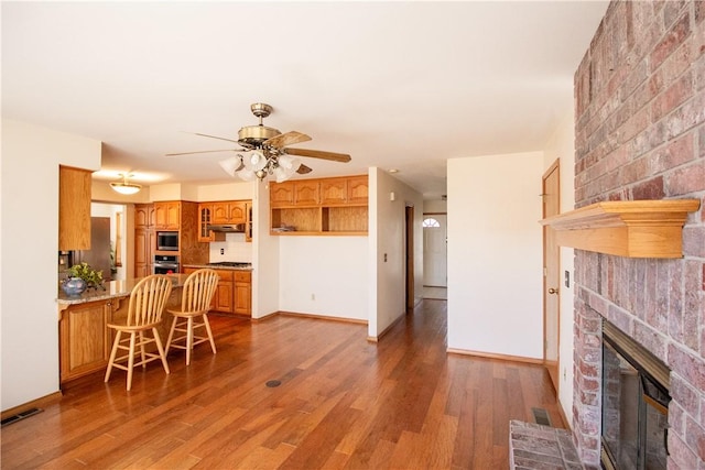 kitchen featuring stainless steel appliances, ceiling fan, hardwood / wood-style flooring, a brick fireplace, and a breakfast bar