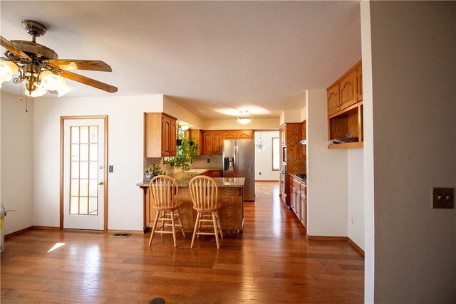 kitchen with a kitchen breakfast bar, stainless steel fridge, dark hardwood / wood-style flooring, and kitchen peninsula