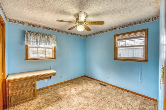 carpeted empty room with ceiling fan, plenty of natural light, and a textured ceiling