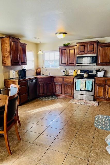 kitchen featuring sink, hanging light fixtures, light tile patterned floors, stainless steel appliances, and backsplash