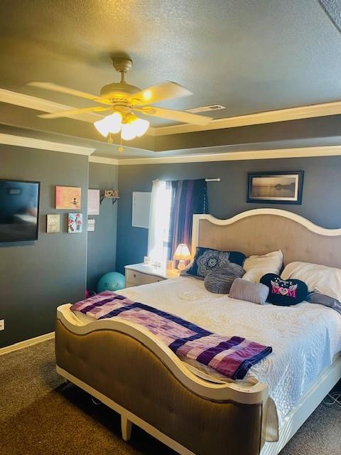 bedroom with ceiling fan, ornamental molding, a textured ceiling, dark carpet, and a raised ceiling