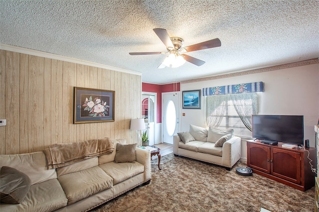 living room with a textured ceiling, wooden walls, carpet, ceiling fan, and crown molding