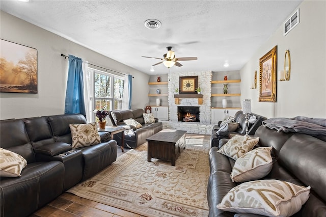 living room featuring a stone fireplace, a textured ceiling, hardwood / wood-style flooring, and ceiling fan