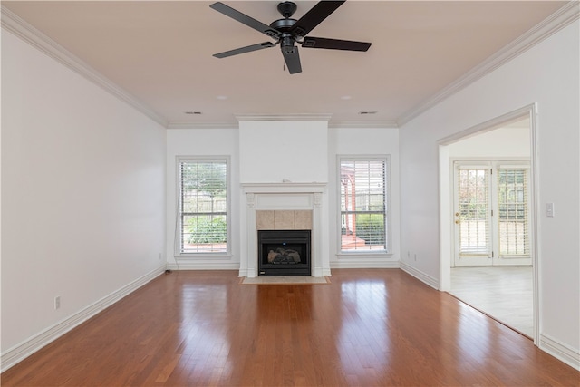 unfurnished living room with light wood-type flooring, a tiled fireplace, ceiling fan, and crown molding