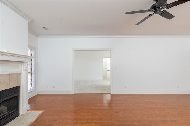 unfurnished living room with ornamental molding, light wood-type flooring, a tiled fireplace, and ceiling fan