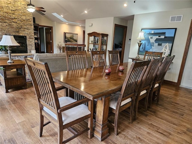 dining space with ceiling fan, a fireplace, wood-type flooring, and lofted ceiling with skylight