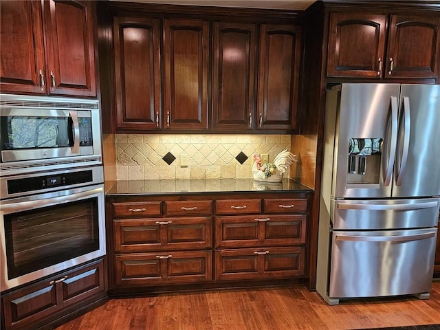 kitchen featuring dark stone countertops, decorative backsplash, stainless steel appliances, and dark hardwood / wood-style floors