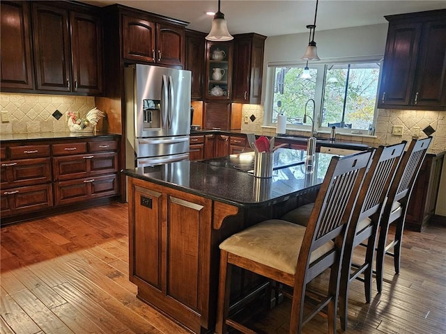 kitchen with hardwood / wood-style floors, a center island, backsplash, stainless steel fridge, and a kitchen bar